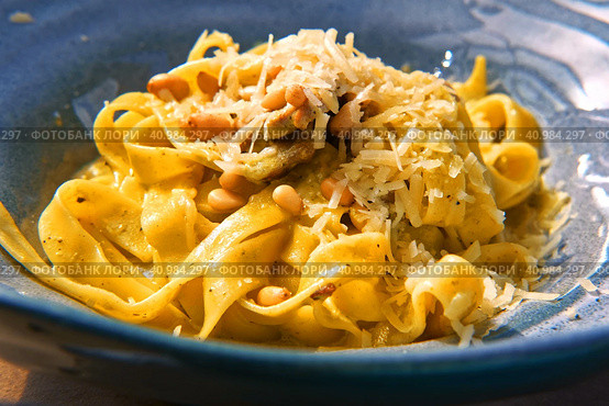Pasta, bavette with nuts, garlic, olive oil. Side view, close-up. Pasta with parmesan cheese. Delicious spaghetti served on a blue ceramic plate. Alfredo pasta dinner, creamy white sauce. Tagliatelle. Стоковое фото, фотограф Марина Демидюк / Фотобанк Лори