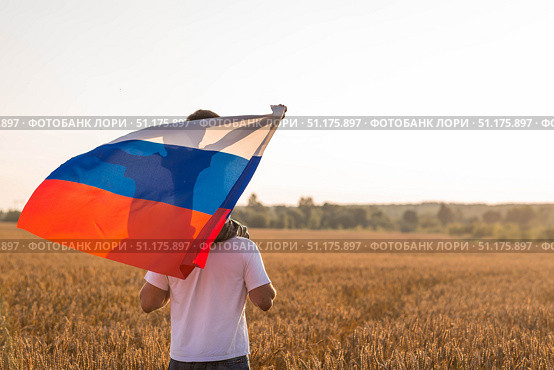 Patriotism. A father and son with the Russian flag in a wheat field at sunset. A family with a flag in nature. The concept of family, cultural values, and a rich harvest of wheat. Стоковое фото, фотограф Photojuli / Фотобанк Лори
