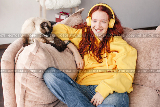 Peaceful teen girl in modern headphones sit relax on comfortable couch listening to music. Стоковое фото, фотограф Гладских Татьяна / Фотобанк Лори