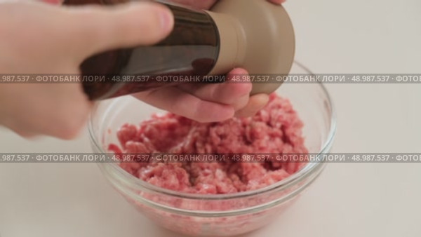 Person seasons raw ground meat with black pepper from a pepper shaker, preparing ingredients for a homemade dish in the kitchen. Стоковое видео, видеограф Андрей Журавлев / Фотобанк Лори