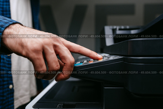 Person uses a multifunction printer to operate photocopying or scanning functions in an office setting during daylight hours. Стоковое фото, фотограф Сергей Толмачёв / Фотобанк Лори