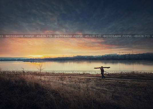 Person walking a country road carrying dry firewood. Peaceful sunset scene and wanderer silhouette on trail. Idyllic rural landscape. Стоковое фото, агентство Ingram Publishing / Фотобанк Лори