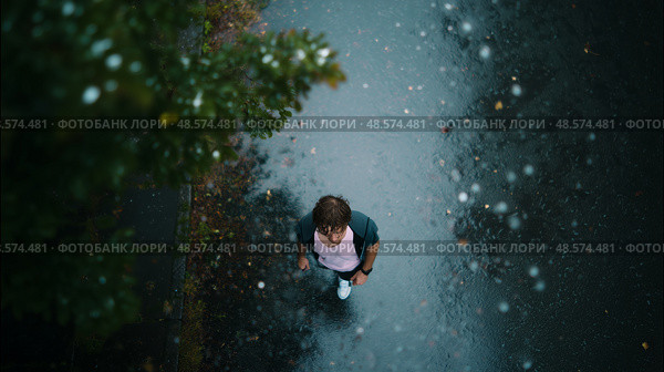 Person walking on a rainy street surrounded by trees during overcast daylight. Стоковое AI-изображение, AI-художник Сергей Толмачёв / Фотобанк Лори