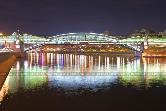 Пешеходный мост Богдана Хмельницкого, ночная подсветка, центр Москвы. Moscow - April 15, 2023. Panorama of Moscow river and Bogdan Khmelnitsky pedestrian bridge with reflection of illuminated buildings. Night sprin view. Стоковое фото, фотограф Александр Кузнецов / Фотобанк Лори