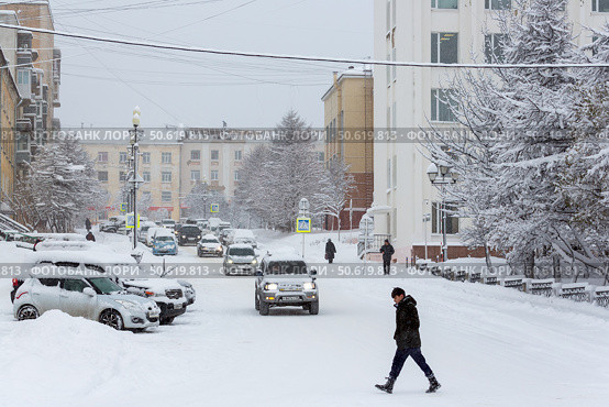 Пешеходы и автомобили на заснеженной городской улице. Много снега на проезжей части, тротуарах и машинах после снегопада и метели. Снежная погода. Магадан, Магаданская область, Россия. (2021 год). Редакционное фото, фотограф Андрей Степанов / Фотобанк Лори