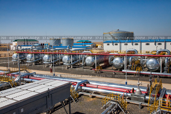 Petrochemical plant. Panorama of oil refinery plant in desert. Heat exchangers, oil storage tanks, pipelines and factory building. Refinery worker in white hardhat and red workwear. Стоковое фото, фотограф Alexey Rezvykh / Фотобанк Лори