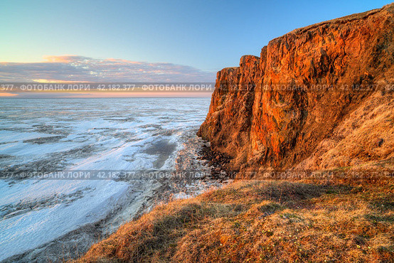 Picturesque arctic landscape. View from the coast to the cape and the frozen sea covered with ice. Beautiful rocks and cliff at sunrise. June in the Arctic. Cape Dionysius, Chukotka, Far East Russia. Стоковое фото, фотограф Андрей Степанов / Фотобанк Лори