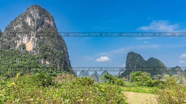 Picturesque mountain landscape. Steep high cliffs against a background of blue sky and clouds. Green vegetation in the valley. China. Yangshuo. Moon Hill. Стоковое фото, фотограф Вера Ивановна Кубарева / Фотобанк Лори