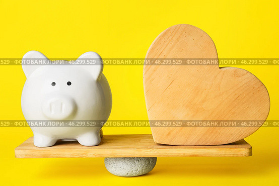 Piggy bank and wooden heart on teeterboard against color background. Concept of balance. Стоковое фото, фотограф Pixel_shot / Фотобанк Лори