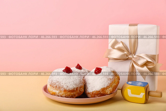 Plate with tasty donuts, dreidel and gift for Hannukah celebration on color background. Стоковое фото, фотограф Pixel_shot / Фотобанк Лори