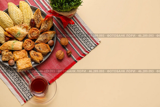 Plate with treats, grass and glass of tea on beige background. Novruz Bayram celebration. Стоковое фото, фотограф Pixel_shot / Фотобанк Лори