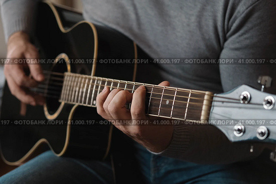 Playing the guitar. Strumming acoustic guitar. Musician plays music. Man fingers holding mediator. Man hand playing guitar neck in dark room. Unrecognizable person rehearsing, fretboard close-up. Стоковое фото, фотограф Марина Демидюк / Фотобанк Лори