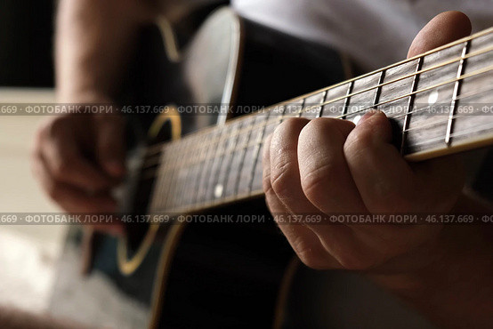 Playing the guitar. Strumming acoustic guitar. Musician plays music. Man fingers holding mediator. Man hand playing guitar neck in dark room. Unrecognizable person rehearsing, fretboard close-up. Стоковое фото, фотограф Марина Демидюк / Фотобанк Лори