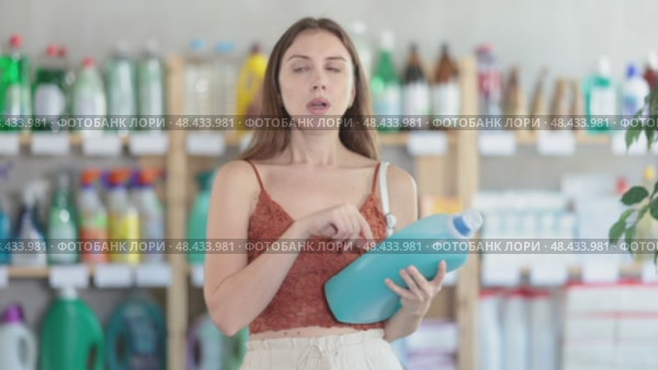 Pleased young girl in summer clothes reviewing washing detergents to buy in supermarket. Стоковое видео, видеограф Яков Филимонов / Фотобанк Лори