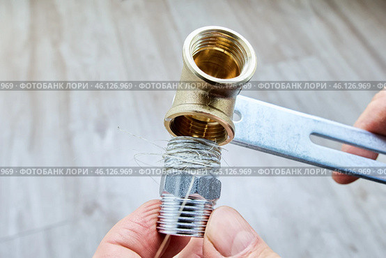 Plumbing flax is wrapped around stainless steel threaded reducer nipple, preparing it for installation into brass pipe fitting. Стоковое фото, фотограф Владимир Григорьев / Фотобанк Лори