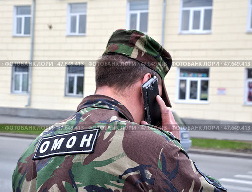 Полицейский в форме стоит спиной и разговаривает по телефону. Надпись "ОМОН" на куртке сзади. Стоковое фото, фотограф Александр Тараканов / Фотобанк Лори