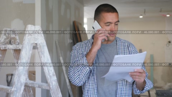 Portrait hispanic man standing on a construction site indoors and having mobile phone conversation about project documentation. Стоковое видео, видеограф Яков Филимонов / Фотобанк Лори