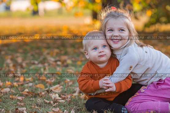 Portrait of a little boy 9 months old and a girl 4 years old outdoors. Happy children are playing in the autumn park. Sister hugs brother. Happy childhood and motherhood. Стоковое фото, фотограф Photojuli / Фотобанк Лори