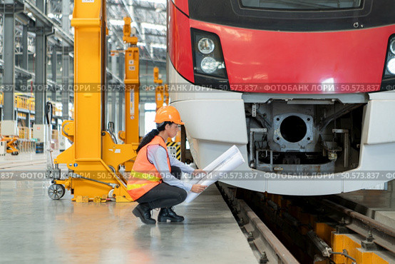 Portrait of a young female technician using a blueprint working and standing in a skytrain repair station. Стоковое фото, агентство Ingram Publishing / Фотобанк Лори