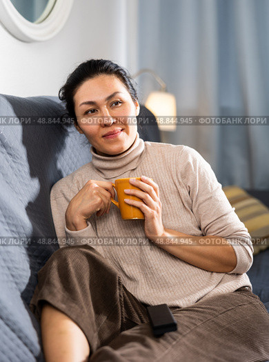 Portrait of an asian woman sitting on a sofa holding a mug. Стоковое фото, фотограф Яков Филимонов / Фотобанк Лори