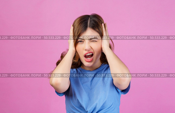 Portrait of angry irritated young woman wearing casual t-shirt covering her ears with hands and shouting while standing isolated over pink background. Expression, people and lifestyle concept. Стоковое фото, агентство Ingram Publishing / Фотобанк Лори