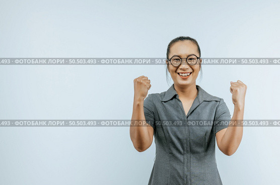 Portrait of Asian woman glasses keeps hands clenched in fists with positiveness as achieved success in career, smiling, showing strong powerful, isolated over background with copyspace. Стоковое фото, агентство Ingram Publishing / Фотобанк Лори