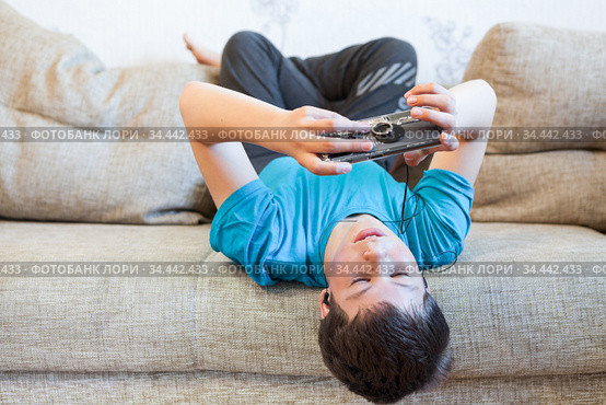 Portrait of Caucasian teenager with large smartphone or game console in hands, playing or engaging over social media while lying his back on sofa. Стоковое фото, фотограф Кекяляйнен Андрей / Фотобанк Лори