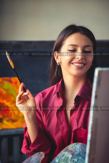 Portrait of perfect young woman painter in red shirt sitting at home studio workshop, smiling look. Happy lovely lady artist paints at canvas with paint oil. Painting at art studio. Copy ad text space. Стоковое фото, фотограф Aleksandr Golubev / Фотобанк Лори