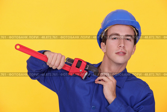 portrait of young plumber holding adjustable spanner against yellow background. Стоковое фото, агентство Ingram Publishing / Фотобанк Лори
