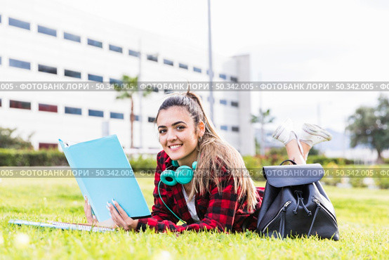 portrait smiling female university student lying green grass holding book hand. Стоковое фото, агентство Ingram Publishing / Фотобанк Лори