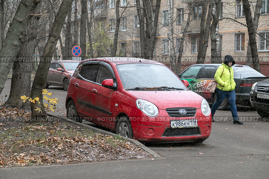 Пошел снег и побелил красный легковой автомобиль во дворе старого пятиэтажного дома. Желтые листья, ноябрь (2022 год). Редакционное фото, фотограф Наталья Николаева / Фотобанк Лори