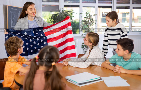 Positive female teacher discussing with preteens students American flag in auditory of middle school. Стоковое фото, фотограф Яков Филимонов / Фотобанк Лори
