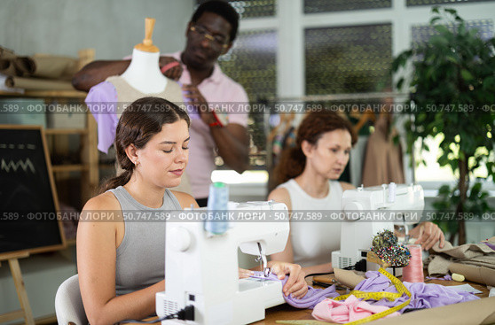Positive girl working at machine during group sewing course for adults. Стоковое фото, фотограф Яков Филимонов / Фотобанк Лори