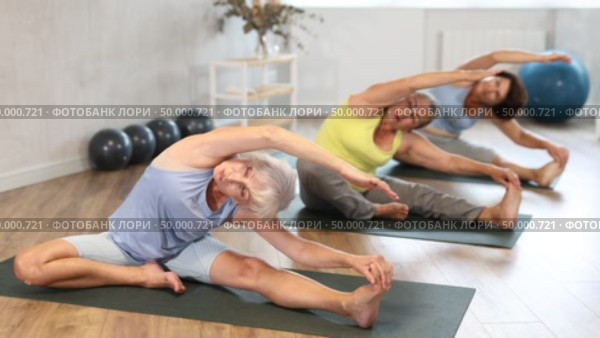 Positive old woman practicing seated side bend pose of yoga on black rug during fitness classes. Стоковое видео, видеограф Яков Филимонов / Фотобанк Лори