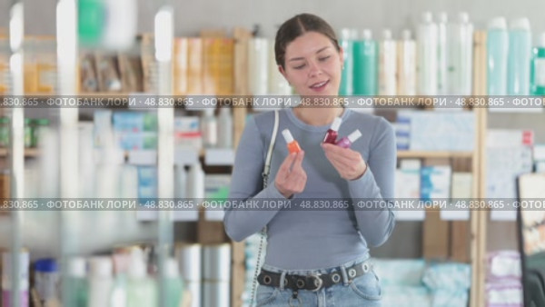 Positive young female customer choosing colorful nail polish in chemist's shop. Стоковое видео, видеограф Яков Филимонов / Фотобанк Лори