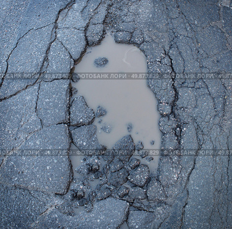 Pot hole or pothole image of a broken cracked asphalt pavement with a dirty water puddle as a transportation symbol of road maintenance and the car insurance risk to auto suspensions. Стоковое фото, агентство Ingram Publishing / Фотобанк Лори