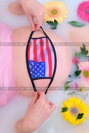 Pregnant woman belly in white bathroom with face mask n95 ffp2 and USA flag. Стоковое фото, фотограф Андрей Журавлев / Фотобанк Лори