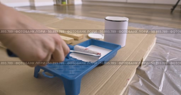 Preparation of paint roller for painting wooden planks, dipping roller in white paint tray. Pouring paint from can into tray close-up of tools, wood board protective film cardboard, renovation process. Стоковое видео, видеограф Сергей Тимофеев / Фотобанк Лори