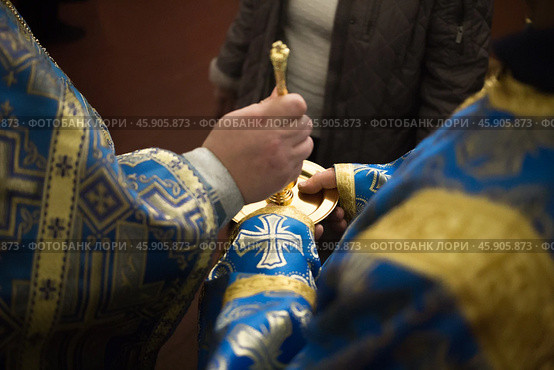 Priest in blue church vestment anoints with sacred oil from golden vessel. Стоковое фото, фотограф irisff / Фотобанк Лори