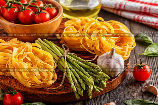 Products for cooking - fresh asparagus, pasta, tomatoes, garlic, olive oil on the old wooden background. Стоковое фото, агентство Ingram Publishing / Фотобанк Лори