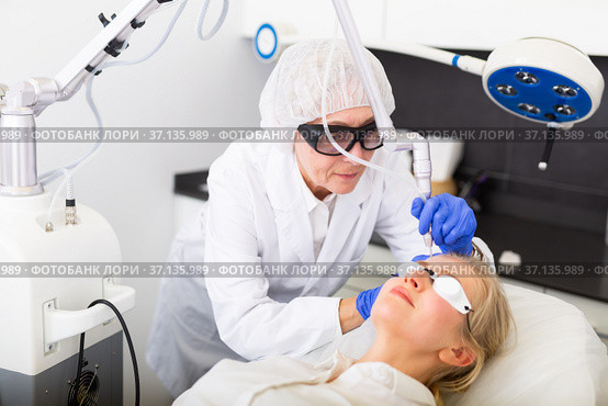 Professional beautician making laser resurfacing to female client face skin. Стоковое фото, фотограф Яков Филимонов / Фотобанк Лори
