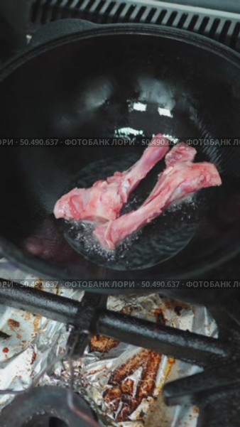 Professional chef wearing protective gloves lowering raw lamb bones into sizzling hot oil, preparing traditional meat dish with skillful culinary technique inside commercial kitchen. Стоковое видео, видеограф Данил Руденко / Фотобанк Лори