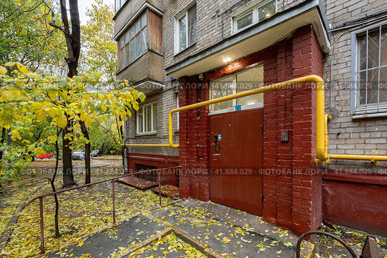 Район Тушино, Москва, Россия, октябрь 2022 года. Вход в подъезд с железной дверью. Желтая труба газоснабжения над дверью. Пятиэтажный кирпичный дом старой хрущевской застройки. Редакционное фото, фотограф Сергей Никифоров-Гордеев / Фотобанк Лори
