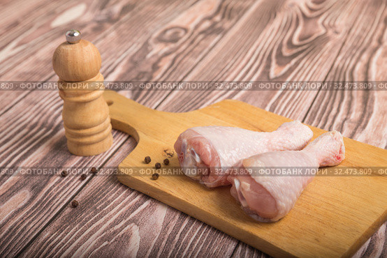 Raw chicken legs on a cutting board and peppercorns with pepper mill. On wooden table. Стоковое фото, фотограф Юлия Бабкина / Фотобанк Лори