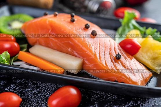 Raw salmon fillets, pepper, kiwi, pineapples, and rosemary onto a plate and black cement floor. Стоковое фото, агентство Ingram Publishing / Фотобанк Лори