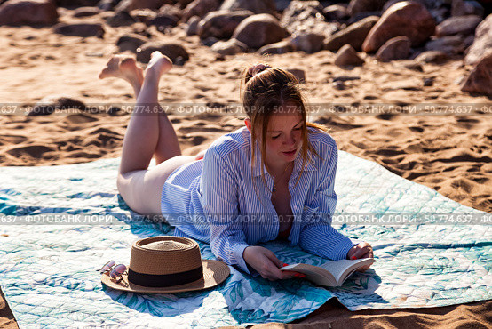 Reading a Captivating Book on a Sunny Beach While Enjoying the Gentle Ocean Breeze. Стоковое фото, фотограф Aleksandr Golubev / Фотобанк Лори