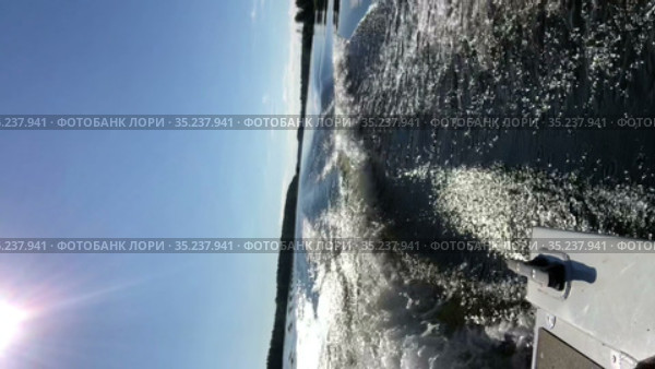 Rear view from riding motorboat, which leaves a wake in the water surface, sunny blue sky on large forest lake. Vertical video. Стоковое видео, видеограф Кекяляйнен Андрей / Фотобанк Лори