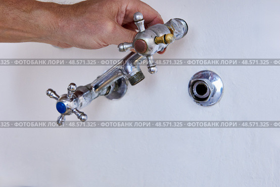 Removing old wall mounted kitchen faucet with two cross handles from hidden pipe in concrete wall, spout already detached, visible hand holding fixture. Стоковое фото, фотограф Владимир Григорьев / Фотобанк Лори