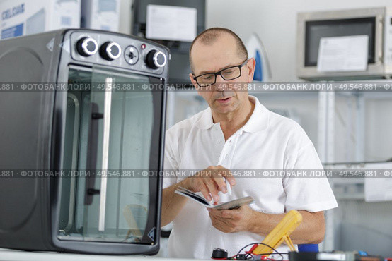 repairman using phone to fix domestic oven in kitchen. Стоковое фото, агентство Ingram Publishing / Фотобанк Лори
