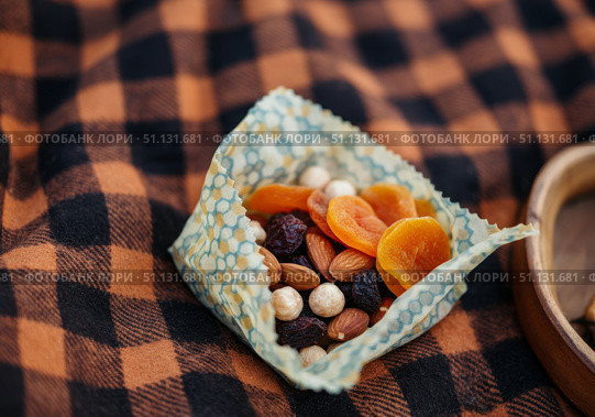 Reusable beeswax wraps with assorted dried fruits on a checkered picnic blanket for eco-friendly storage. Стоковое AI-изображение, AI-художник Гайфуллина Дина / Фотобанк Лори